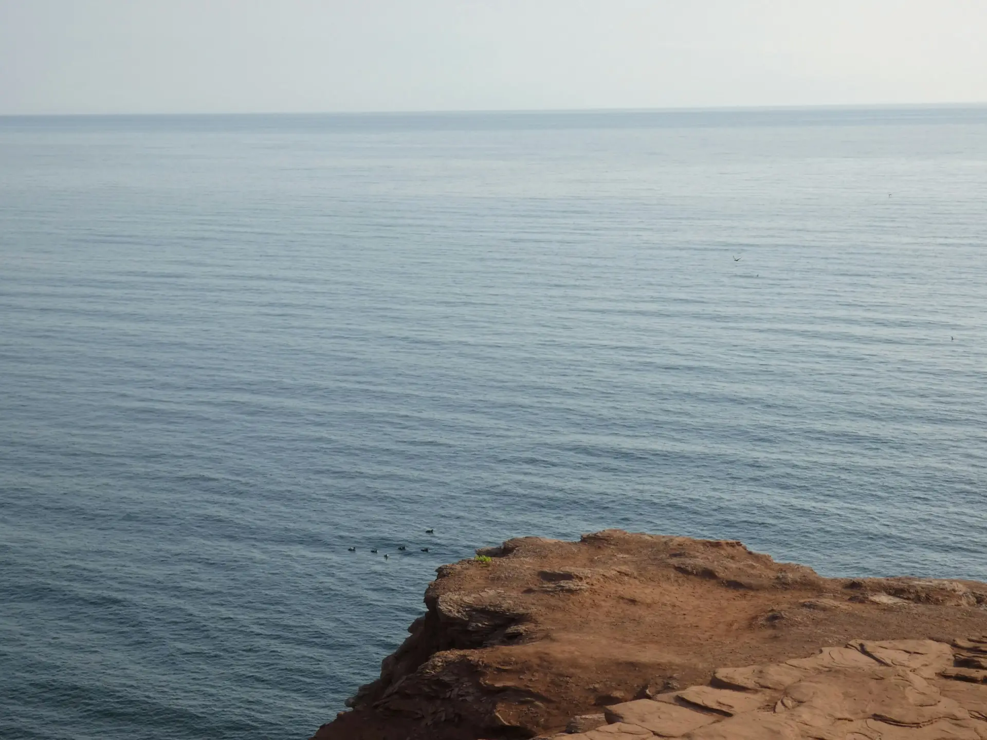 El mar Mediterráneo en calma visto desde una plataforma de roca al borde del acantilado, con la línea del horizonte difuminada por la bruma.